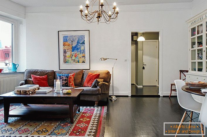 Стильна кімната для гостей в звичайній міській квартирі декорована яскравими подушками на дивані і килимом. 