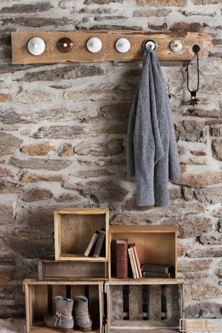Сільський DIY гардероб в номері з кам'яною стіною; шпильки, виготовлені з старих фарфових кришок та старих дерев'яних ящиків на підлозі, як зберігання