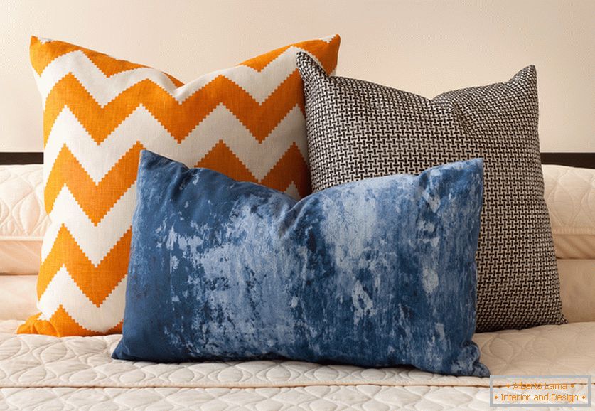 Яскраві помаранчева, синя і чорно-біла декоративні подушки з цікавими принтами на ліжку