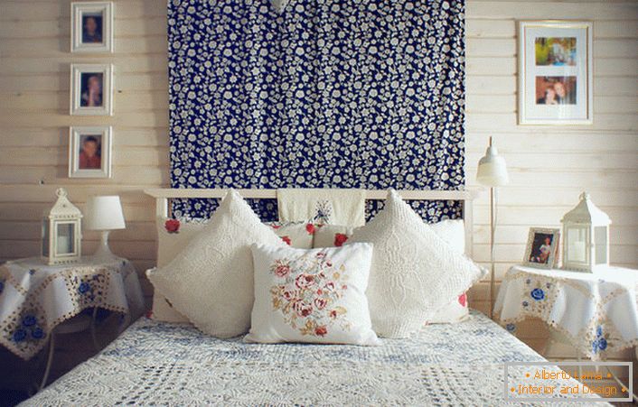 Відповідно до сільським стилем ліжко прикрашає безліч подушок з контрастною вишивкою червоного кольору. Приліжкові столики накриті скатертиною з ніжними блакитними квітами.