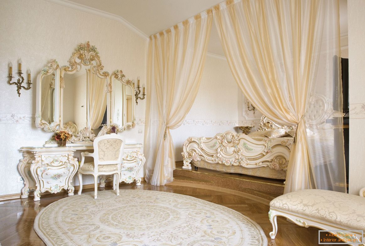 Обрамлення дзеркал і декоративні елементи меблів виконані в одному стилі з використанням золота. З метою економії простору ліжко захована в нішу, обрамлену шторами.
